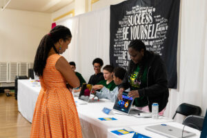 A guest listens to a DDI student as she showcases her website.
